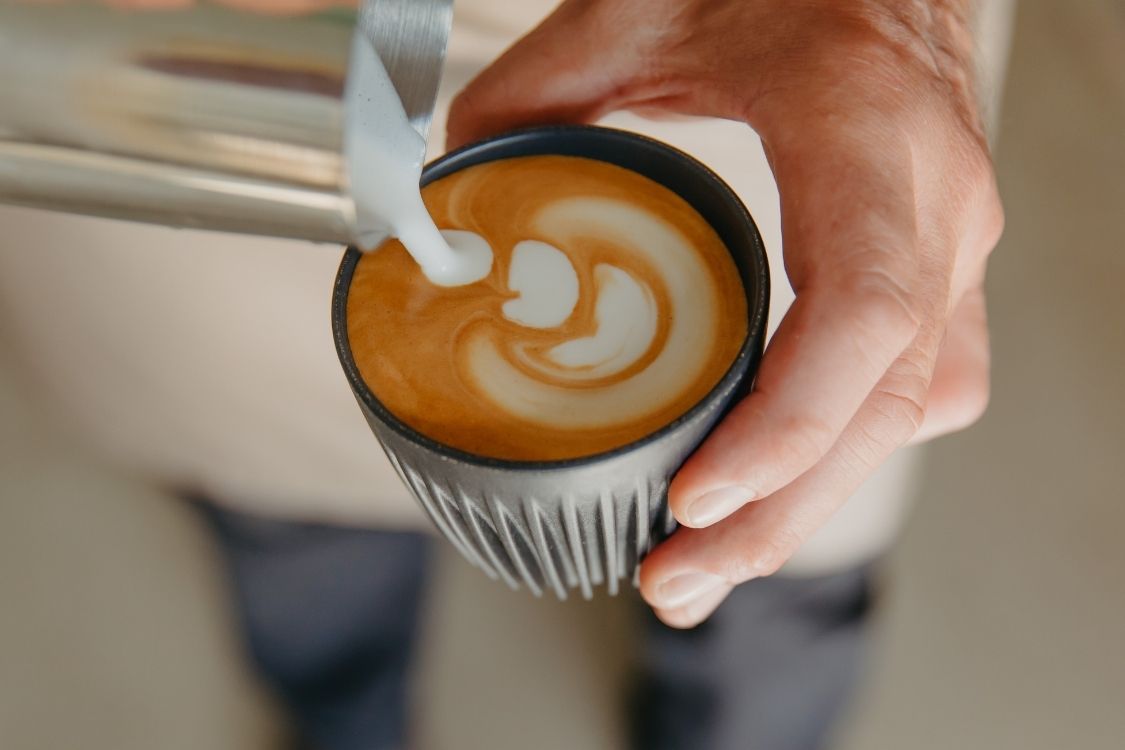 Barista pouring milk from a metallic jug into a coffee cup
