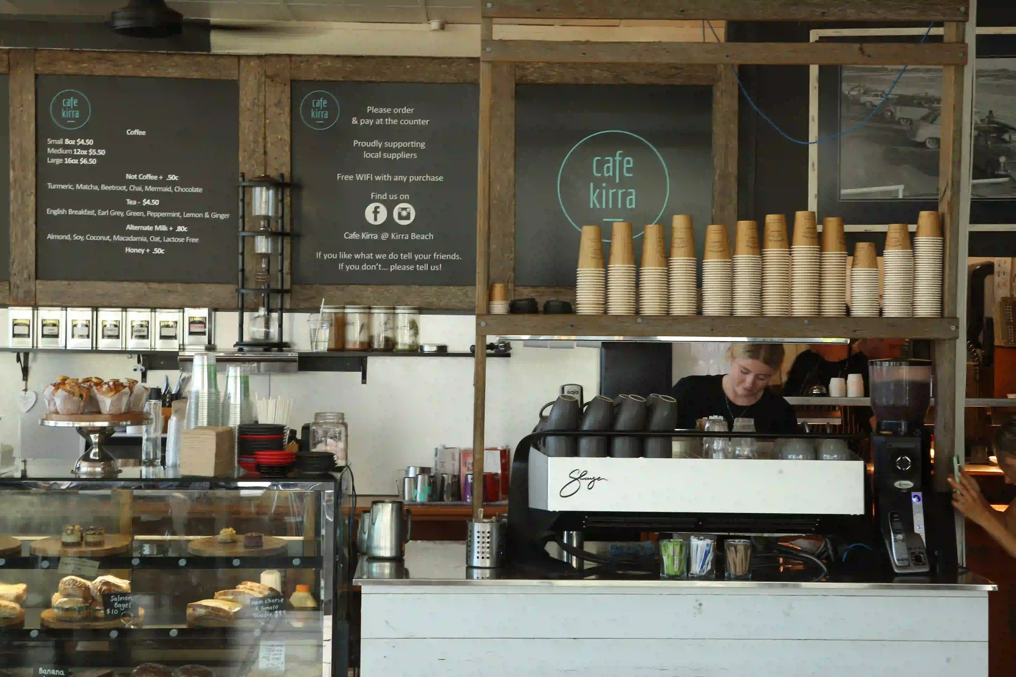 Coffee shop interior with a counter, shelves, and a person behind the counter.