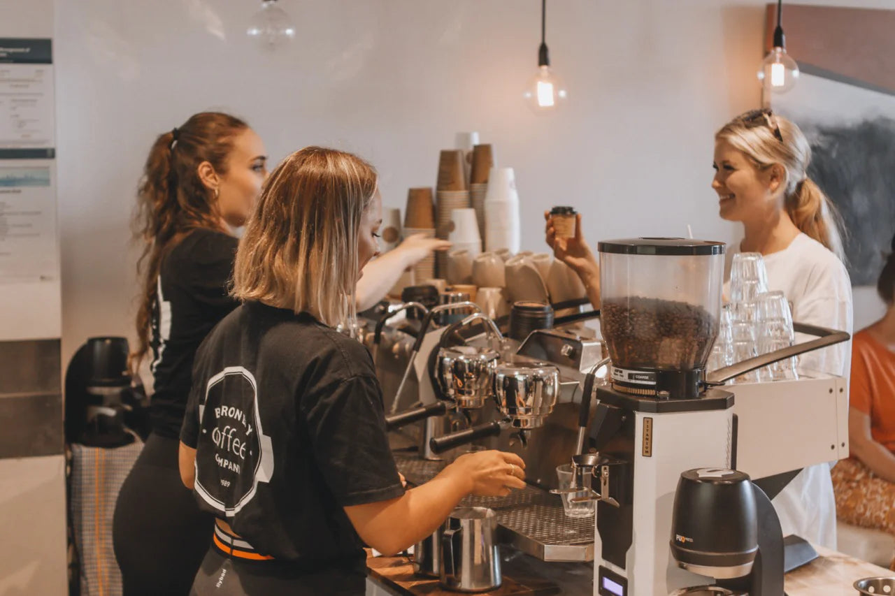 Three women working behind a coffee counter in a cafe.