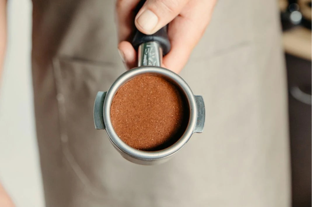 Hand holding a portafilter filled with ground coffee