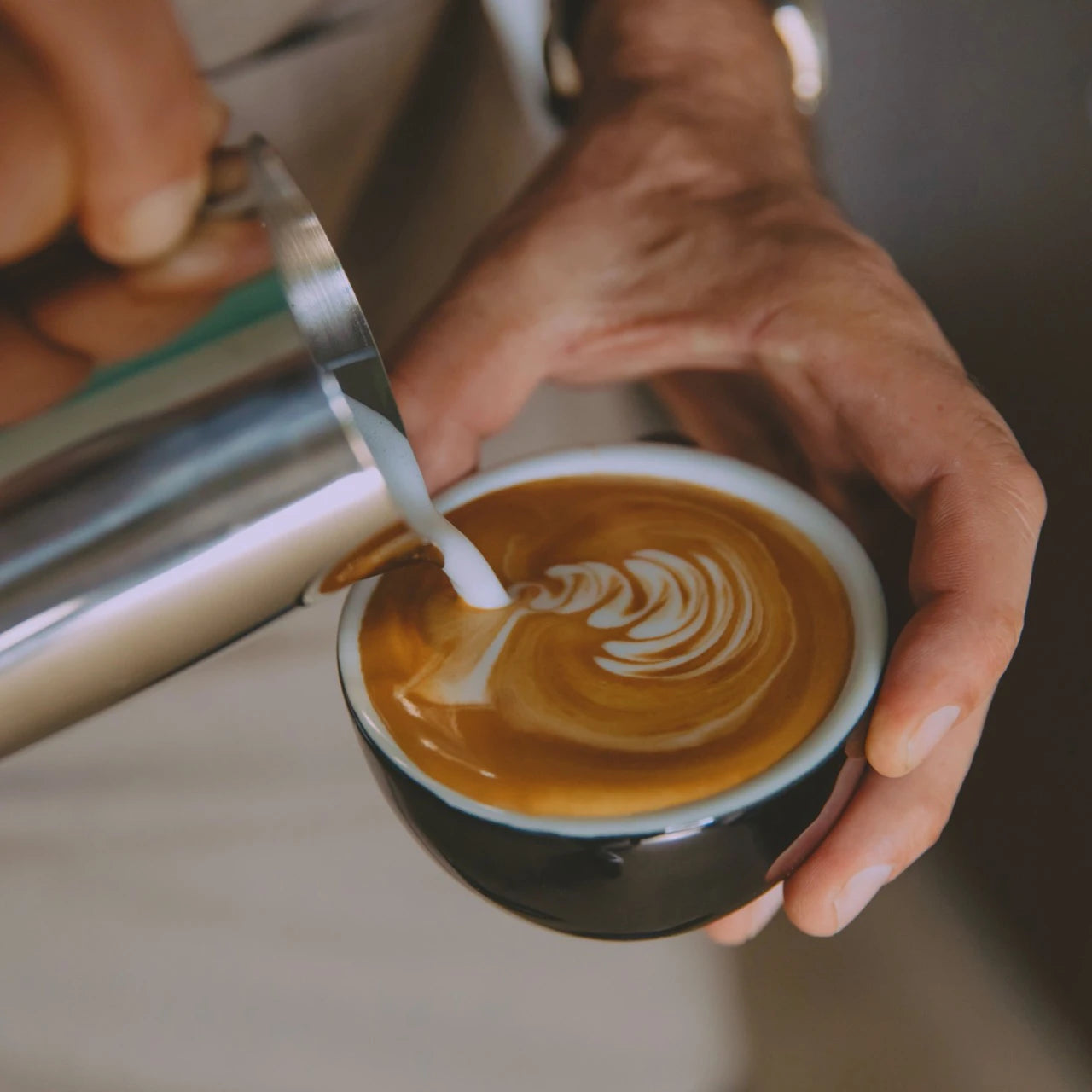 Person pouring milk into a cup of coffee to create latte art.
