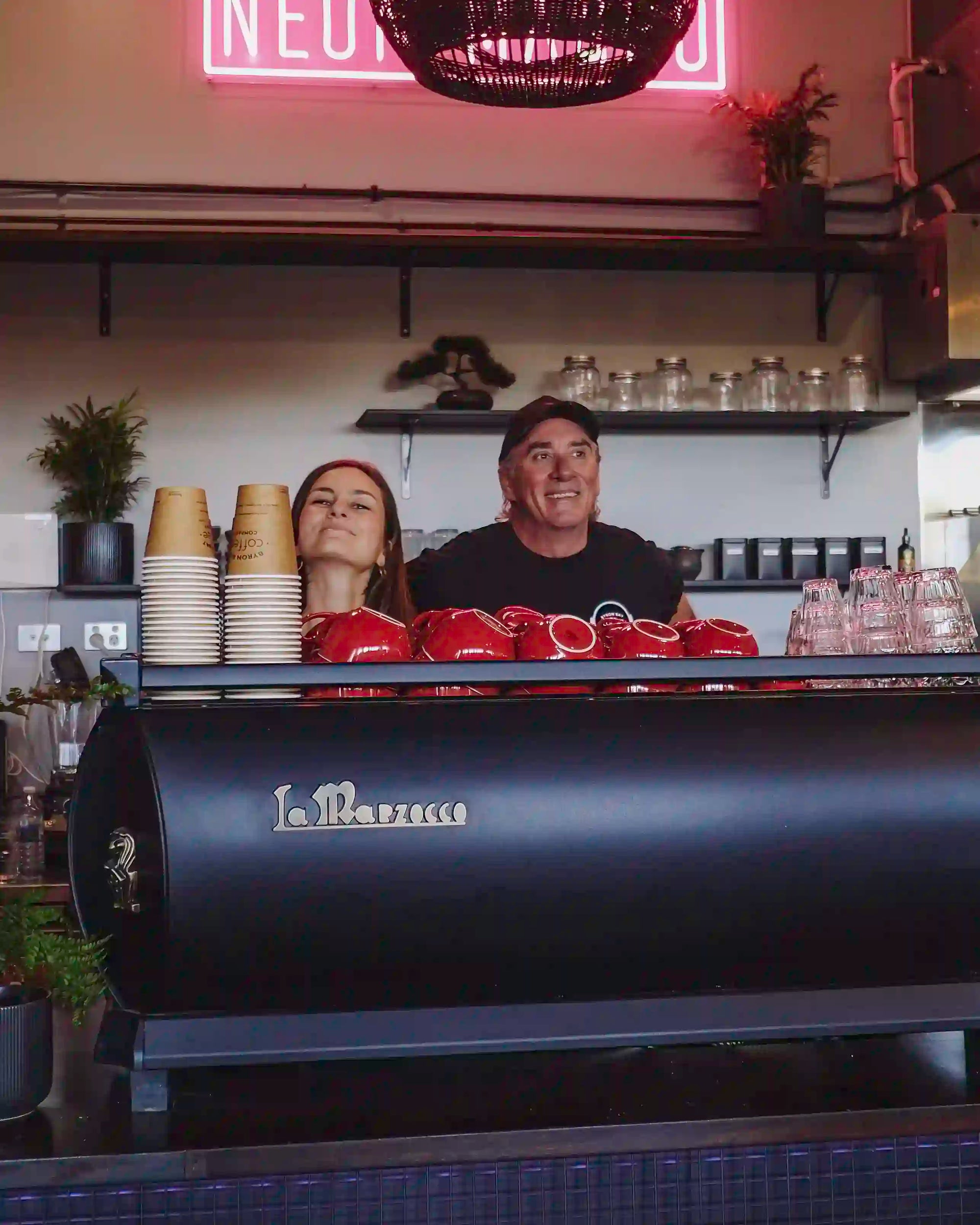 Two baristas behind a counter with a La Marzocco coffee machine in a coffee shop.