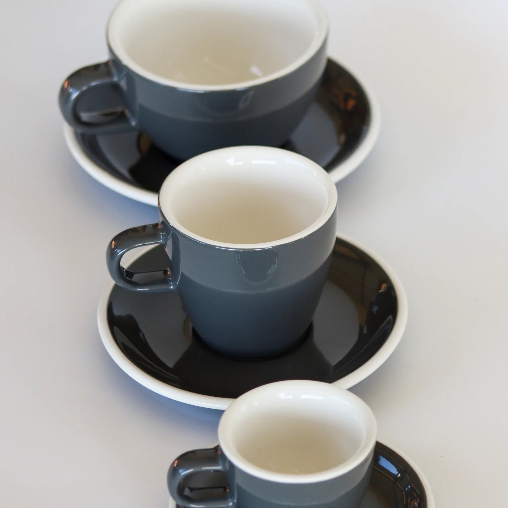 3 sizes of grey ceramic ACME branded cups and saucers