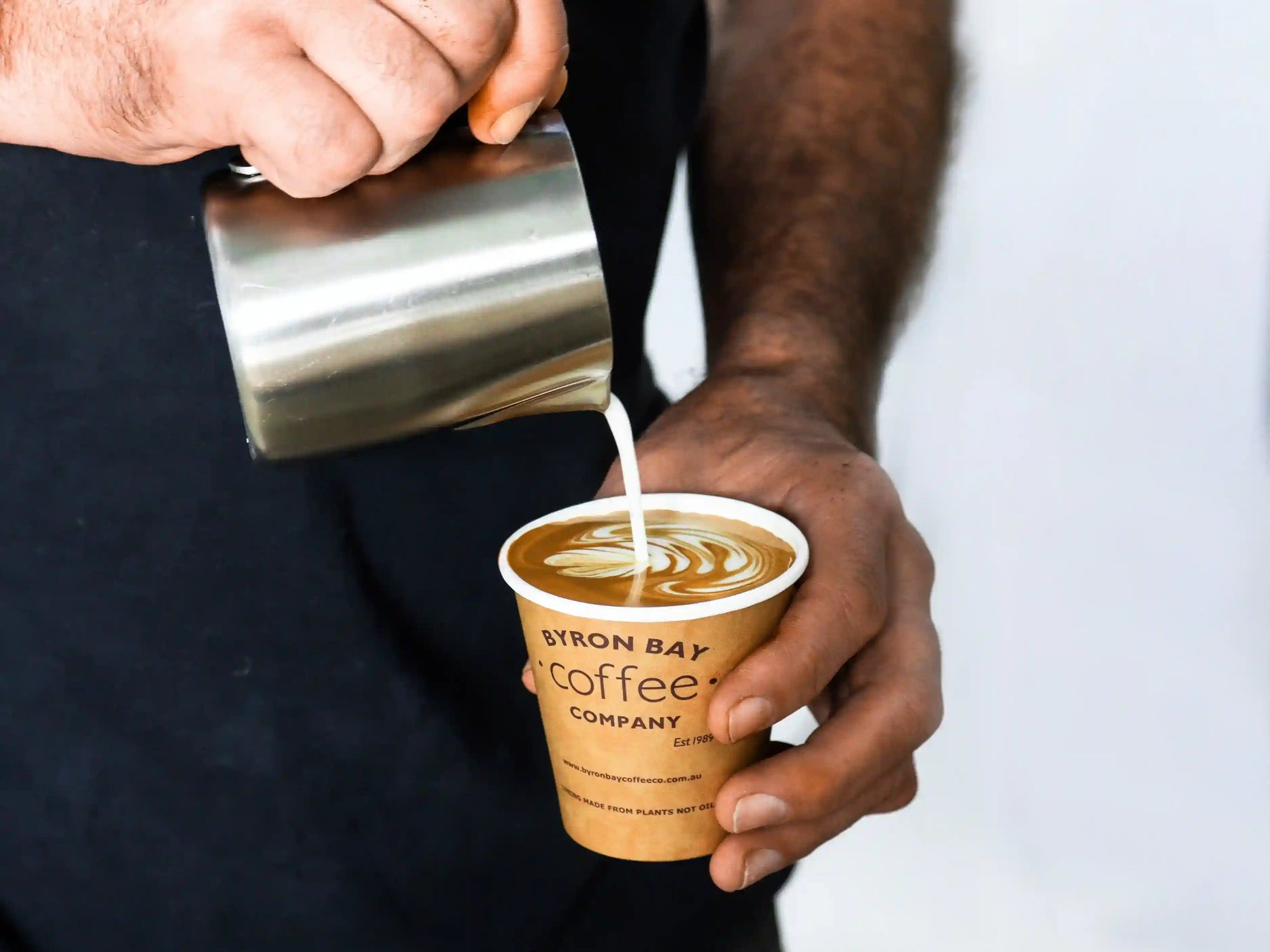 Person creating latte art into a Byron Bay Coffee Company cup